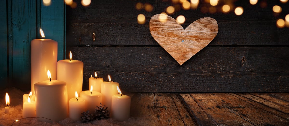 Burning candle on dark wood table with warm golden bokeh light and green shutters in the background