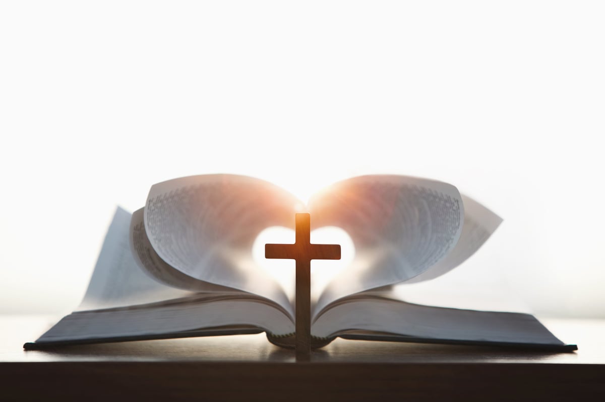 Open Bible with a heart-shaped glow and a cross in the background on a warmly lit wooden surface