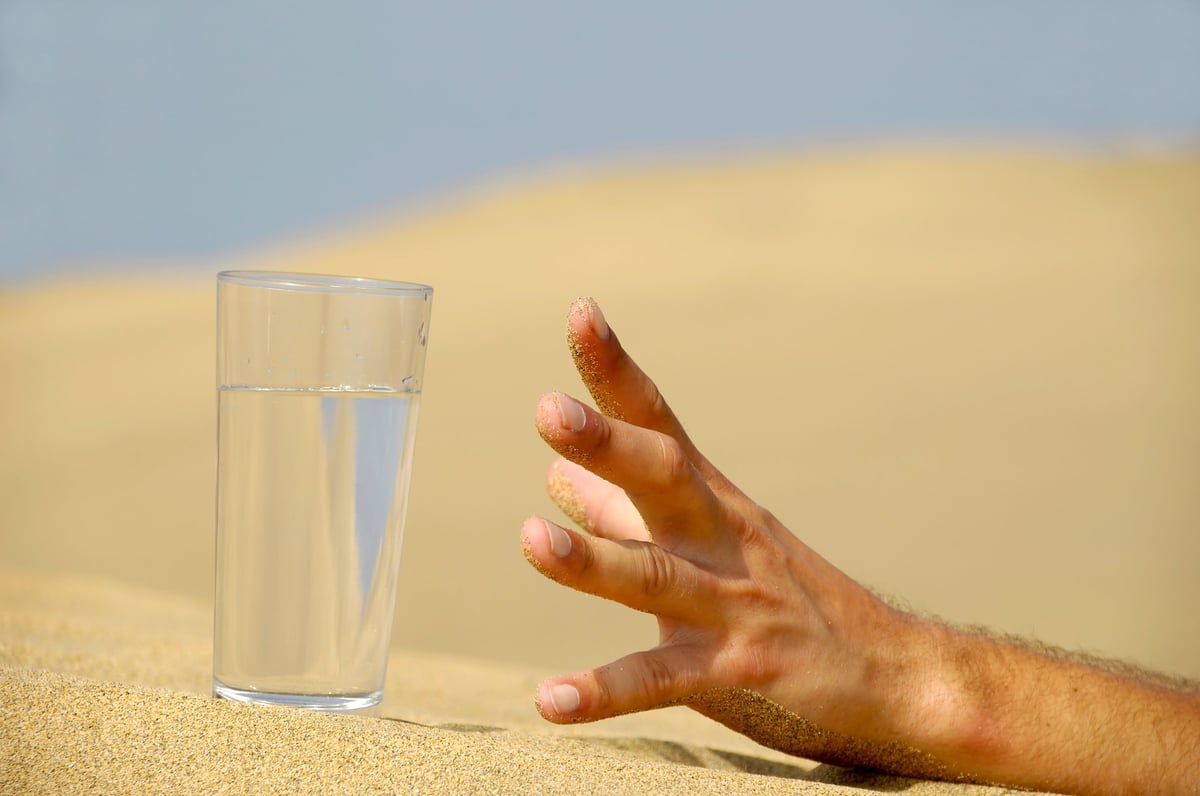 A parched hand reaching toward water in the desert